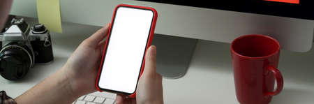 Cropped shot of female photographer using mock-up smartphone while sitting at comfortable workspace...