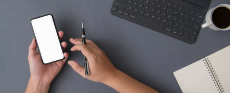 Overhead shot of businessman using mock-up smartphone while working with digital tablet and stationery on grey tableの写真素材