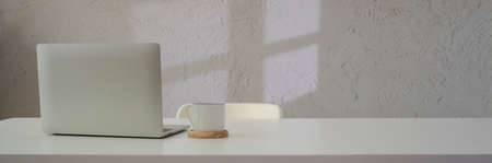 Close up view of simple workspace with laptop, coffee cup and copy space on white table with chairの写真素材