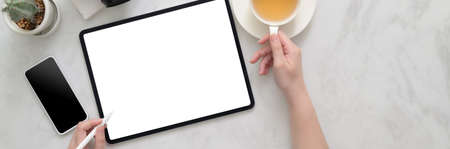 Overhead shot of female freelancer working on mock-up tablet on marble table with tea cup and smartphone in home officeの写真素材