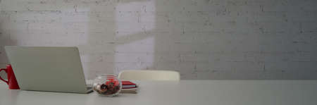 Cropped shot of stylish workspace with laptop, notebooks, coffee mug and copy space on white table with white chair の写真素材