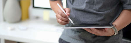 Cropped shot of male entrepreneur working on blank screen tablet with stylus while standing at...