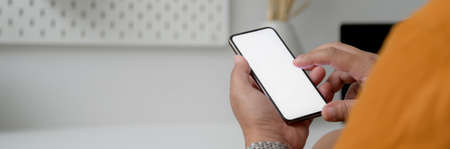 Cropped shot of male freelancer touching on mock-up smartphone while sitting at home office 