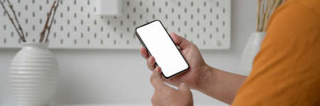 Close up view of male freelancer touching on mock-up smartphone while sitting at home office 