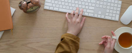 Overhead shot of college student doing her assignment with computer device on wooden table with tea...