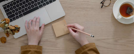 Overhead shot of female freelancer working on laptop while sitting in autumn workspace with tea cup...