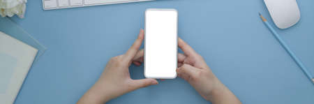 Overhead shot of female freelancer working from home on blank screen smartphone on light blue table with suppliesの写真素材
