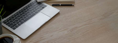 Cropped shot of simple workspace with laptop, coffee cup and copy space on wooden table background  