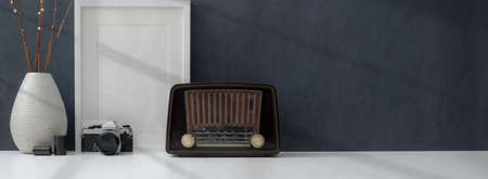 Cropped shot of dark stylish workplace with mock up frame, vintage radio and decorations on white tableの写真素材