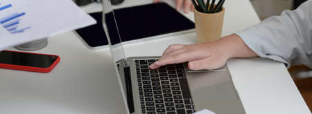 Side view of businesswoman typing on laptop on white table with other digital devices and office...