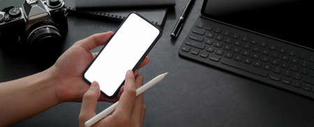 Cropped shot of male entrepreneur using mock-up smartphone while working with digital tablet, camera...