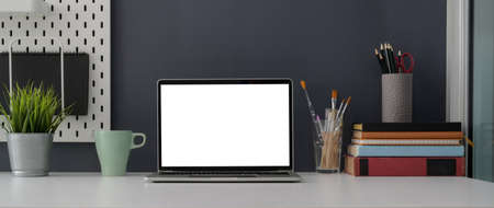 Close up view of home office desk with blank screen laptop, supplies and decorations on white table...
