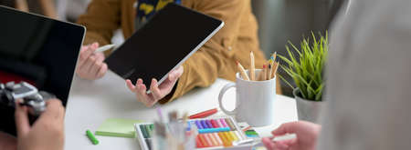 Cropped shot of designer team consulting on their project with digital tablet, camera and designer supplies in minimal workspaceの写真素材