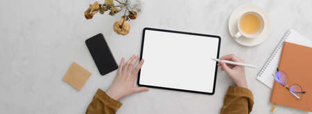 Overhead shot of college student doing an assignment with mock-up tablet, smartphone, supplies and tea cup on marble tableの写真素材