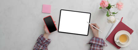 Top view of female freelancer working on  blank screen tablet and smartphone on marble desk with...