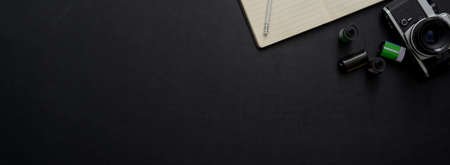 Top view of dark concept office desk with camera, notebook and copy space on black tableの写真素材