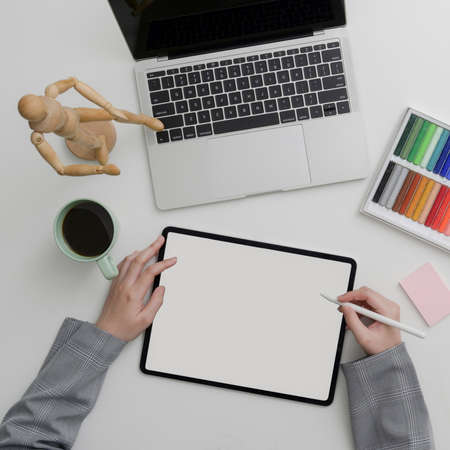 Top view of female designer woking with digital devices and designer supplies on marble table