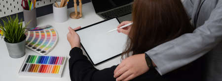 Cropped shot of female designer working on mock-up tablet with stylus pen while consulting with her colleague in trendy workplaceの写真素材