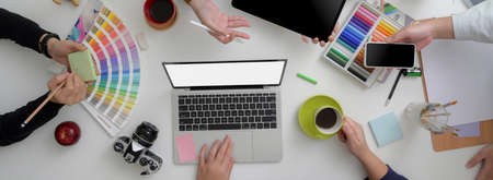 Designer team consulting on their project in minimal meeting room with mock-up laptop, tablet, smartphone and designer supplies on white table   の写真素材