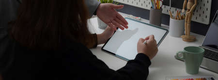 Cropped shot of female designer working on mock-up tablet while consulting with her colleague in modern workplaceの写真素材