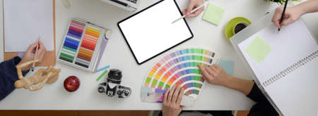 Top view of designer team brainstorming on their project in minimal workspace with mock-up tablet and designer supplies on white table   の写真素材