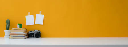 Close up view of creative workspace with camera, books, cactus pot and copy space on white table with yellow wallの写真素材