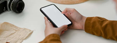 Cropped shot of female photographer using mock-up smartphone to contact customer on white table with suppliesの写真素材