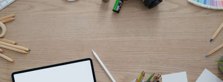 Overhead shot of artist workspace with blank screen tablet, painting tools, notepad and copy space on wooden desk   の写真素材