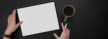 Overhead shot of female freelancer working on mock-up tablet with stylus pen and coffee cup at dark modern workspaceの写真素材