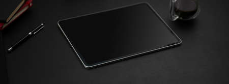 Cropped shot of dark modern workspace with digital tablet, coffee cup and other supplies on black table  の写真素材