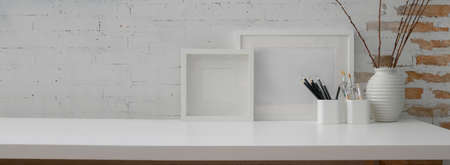 Close up view of contemporary workspace with mock-up frames, stationery, decoration and copy space on white table with brick wall の写真素材