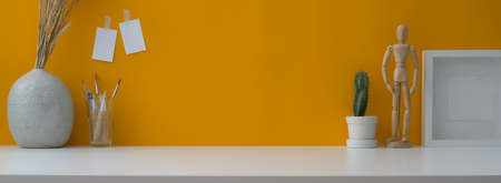 Close up view of creative workspace with copy space, decorations, painting tool on white table with yellow wall の写真素材