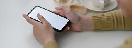 Side view of female freelancer using mock-up smartphone to contact customer on white table with...