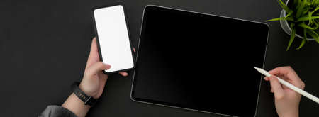 Overhead shot of female freelancer working on digital tablet with stylus pen and mock -up smartphone...