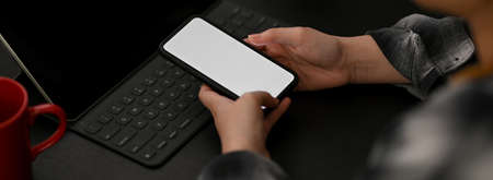 Close up view of female entrepreneur working at dark modern office desk with mock-up smartphone and...