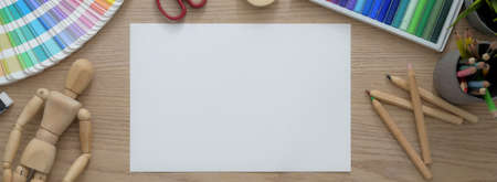 Top view of artist workspace with sketch paper, painting tools and decorations on wooden desk 