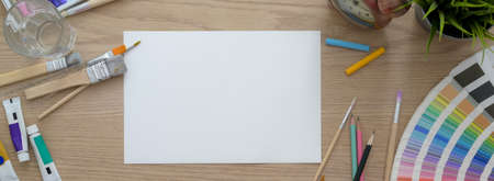 Overhead shot of artist workspace with sketch paper, painting tools and decorations on wooden desk 