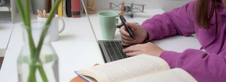 Close-up view of young girl studying on her final exam in comfortable room while typing on laptop...
