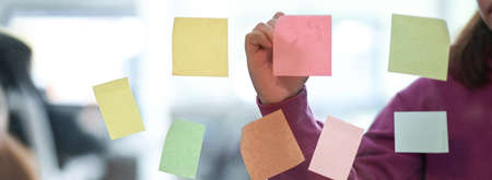 Close up view of female college student  preparing her presentation with sticky note to remind on glass wallの写真素材