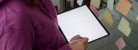 Side view of female college student  preparing her presentation with mock-up tablet and sticky note...