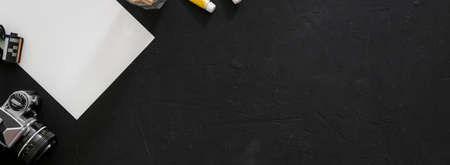 Top view of artist workspace with sketch paper, painting tools, camera and copy space on black tableの写真素材