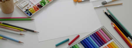 Top view of artist workspace with sketch paper, oil pastels, painting tools and copy space on white desk の写真素材