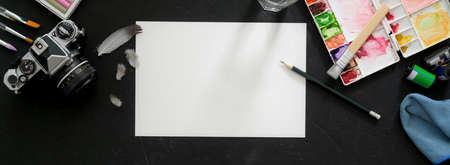 Top view of artist workspace with sketch paper, painting tools, camera and other supplies on black tableの写真素材