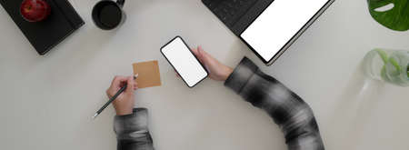 Overhead shot of businesswoman noting an idea on sticky note while looking informations on mock-up...