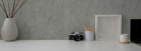 Close up view of modern workspace with camera, laptop, decoration and copy space on white table with loft wallの写真素材