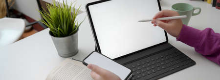 Cropped shot of young college girl doing her assignment with mock-up digital devices and book on...