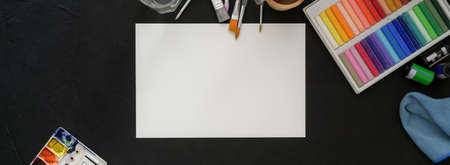 Top view of artist workspace with sketch paper, oil pastels and painting tools on black table  の写真素材