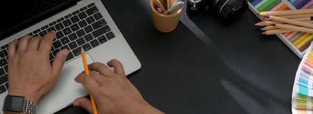 Top view of graphic designer working on laptop on black worktable with designer supplies and copy...