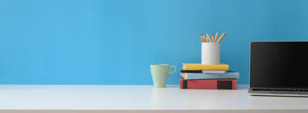 Close up view of creative workspace with laptop, books, stationery, mug and copy space on white...