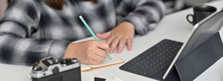 Cropped shot of female freelancer taking short note on blank notebook while looking information on...